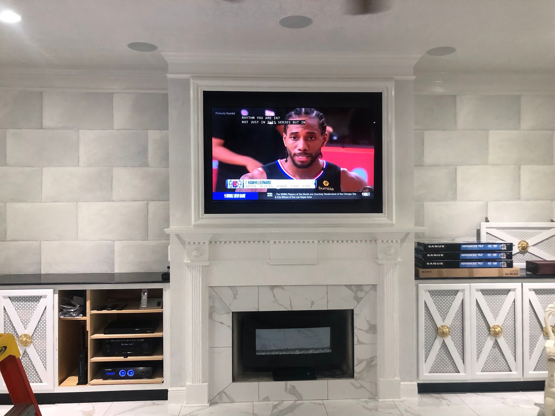 TV mounted above a fireplace, white and gray decor, with a basketball game on screen.