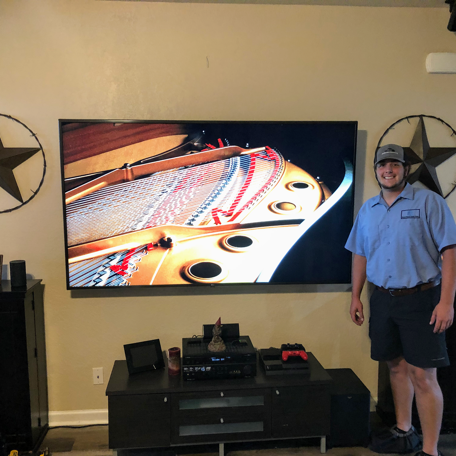 Man stands next to a large TV displaying a close-up of a piano. Black media console below.