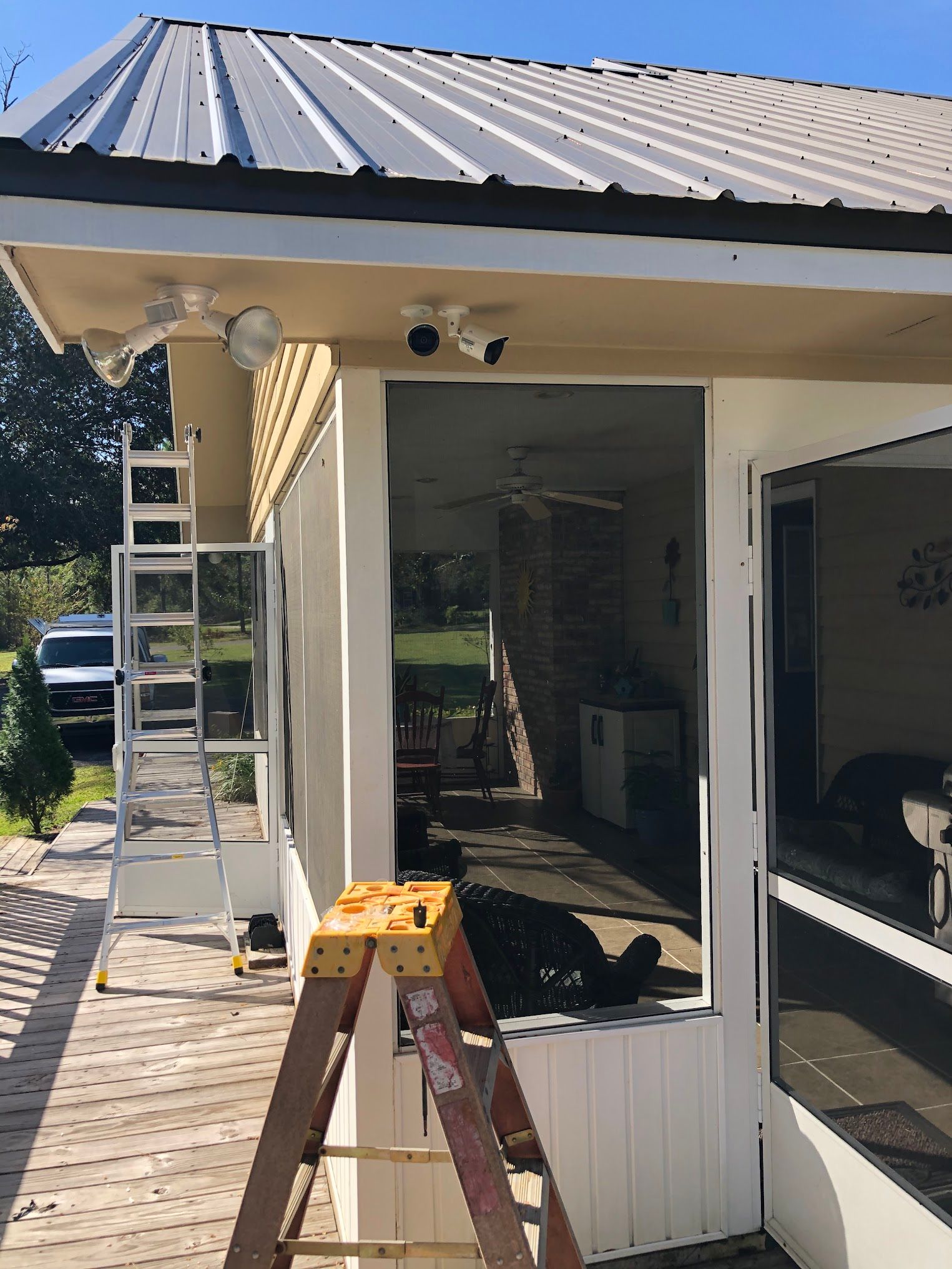 Two ladders at a building exterior. Security cameras mounted. White walls, gray roof, open screened door.