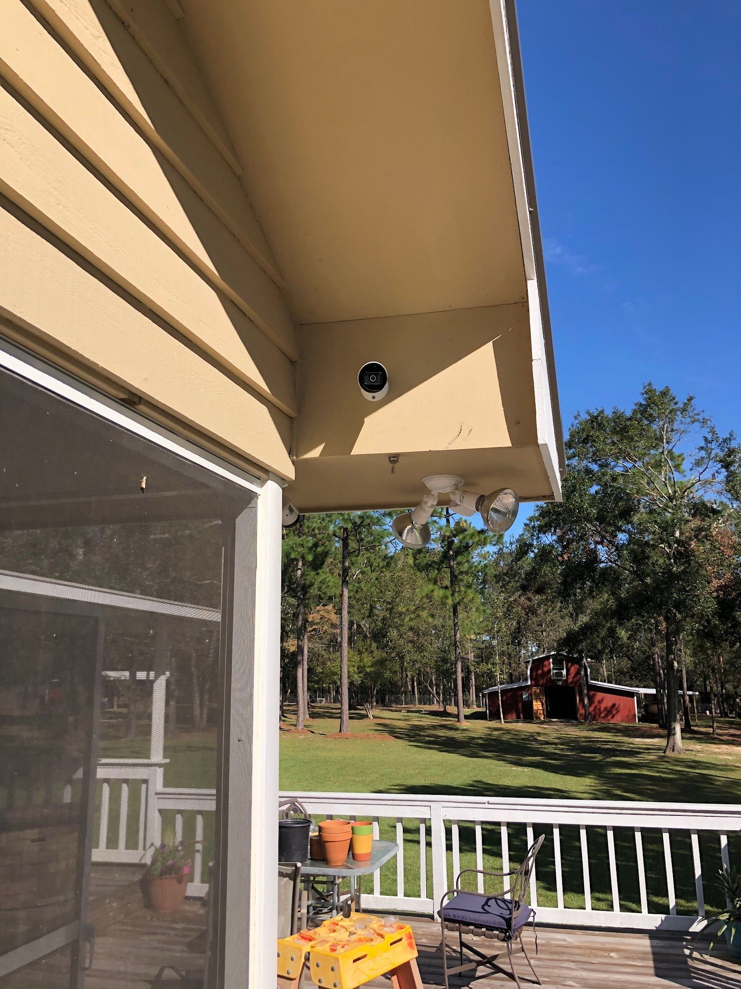 Beige house corner with security camera and floodlights; screened porch and backyard visible.