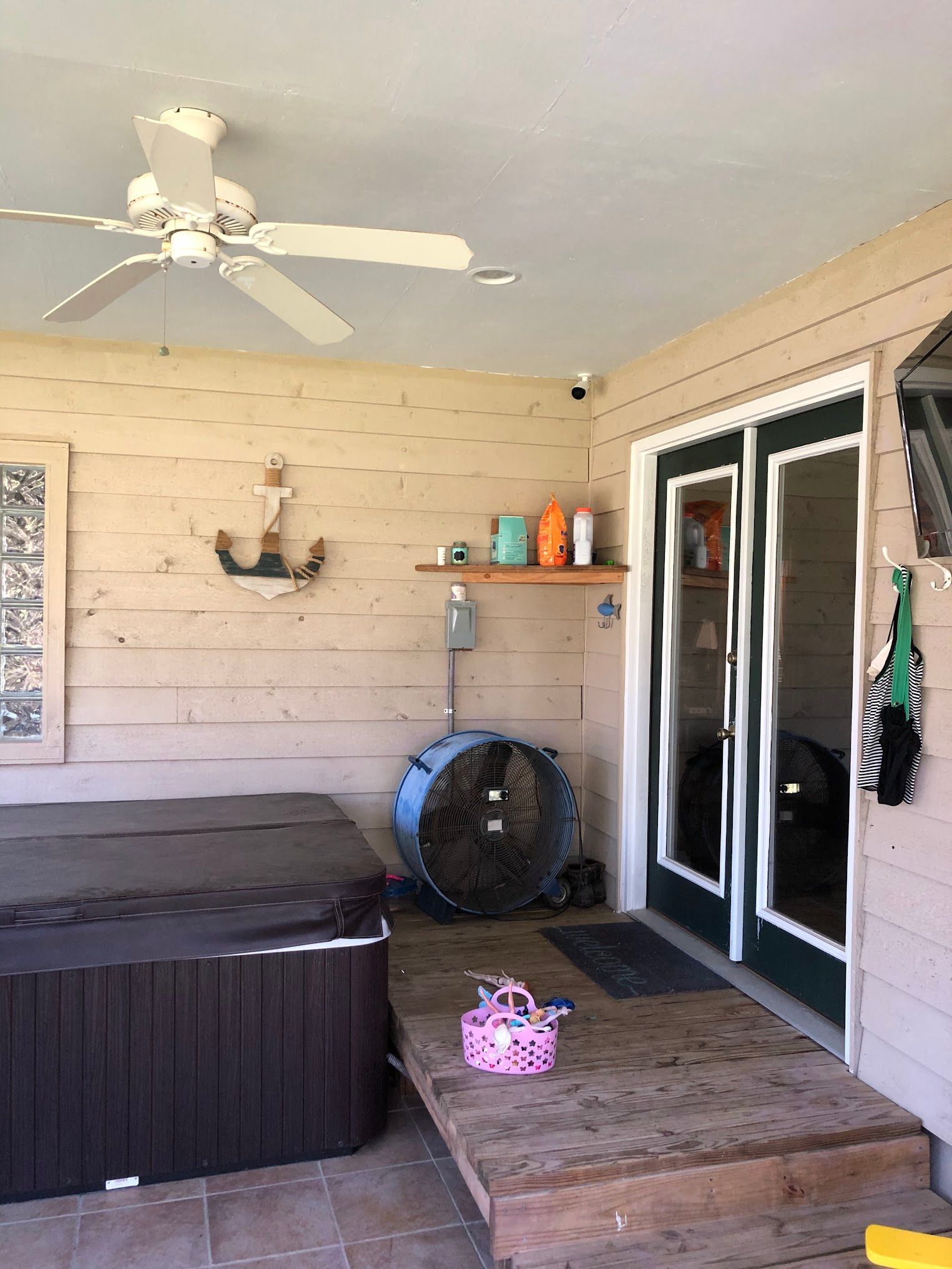 Covered outdoor space with hot tub, double doors, and a fan.