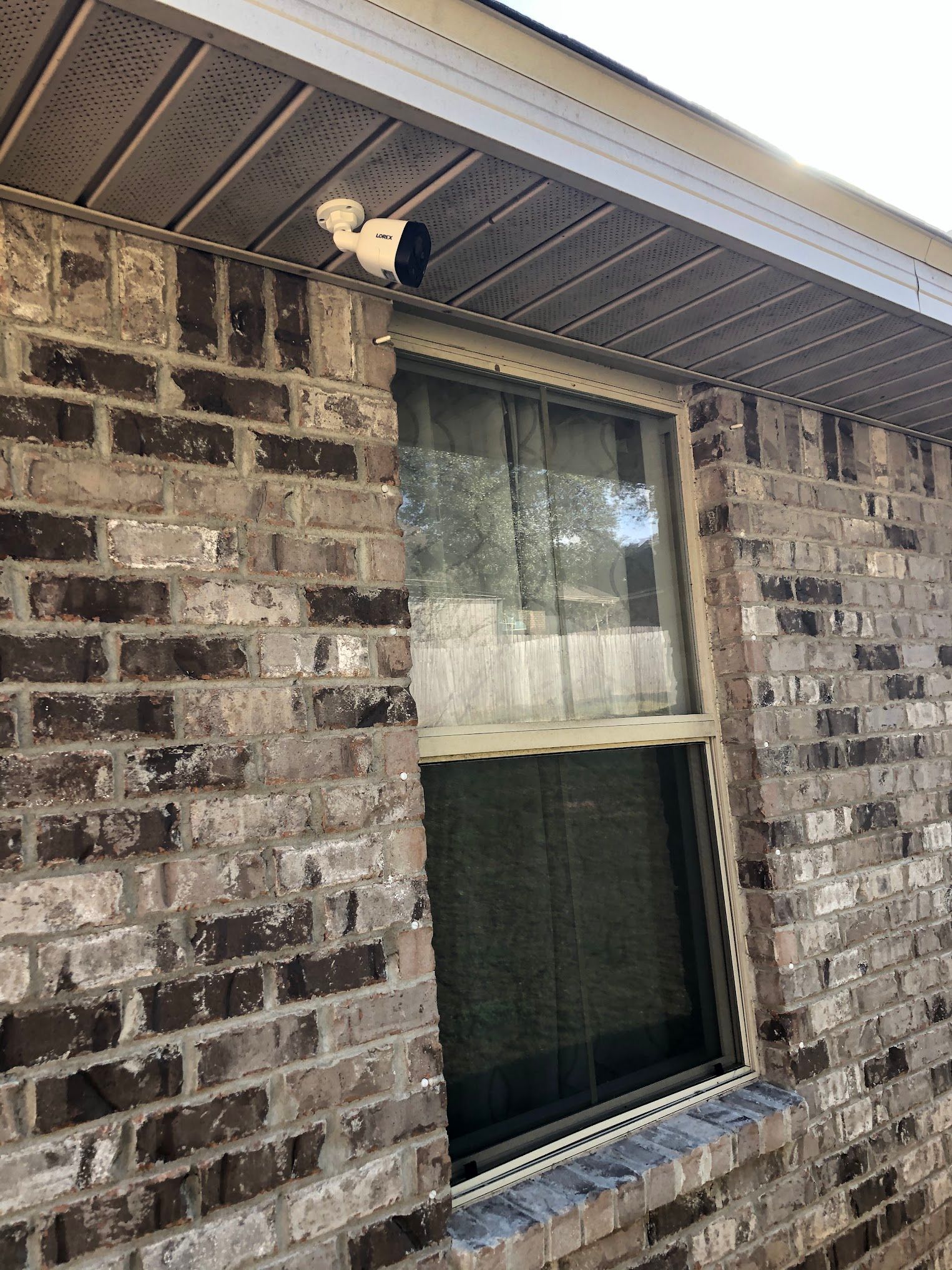 Security camera mounted above a window on a brick wall.