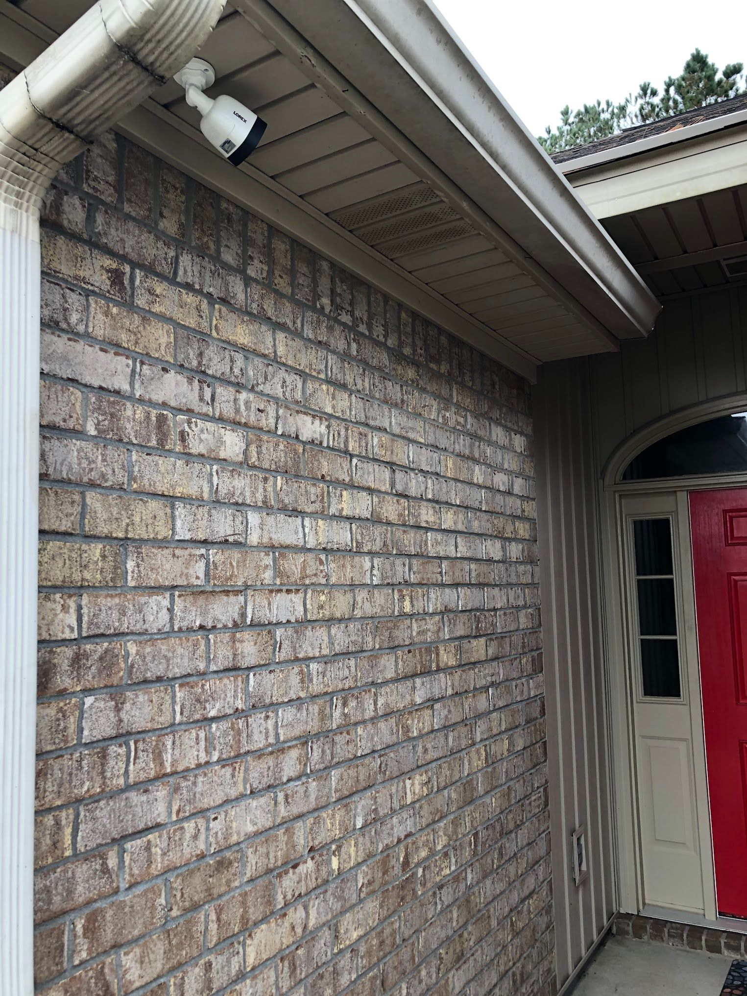Security camera mounted on a brick exterior wall near a gutter and red door.