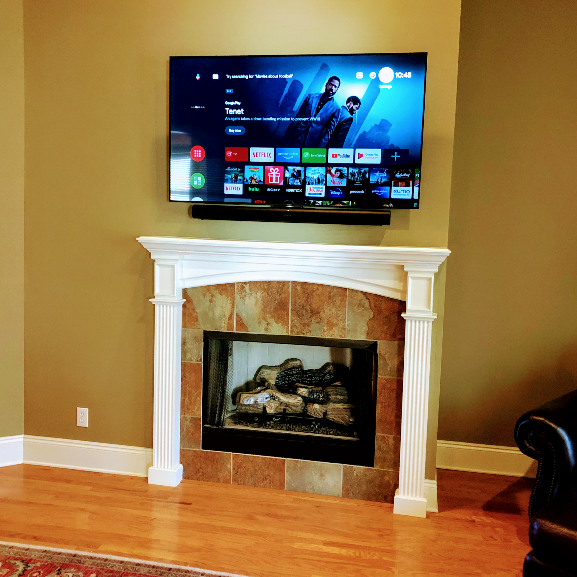 TV mounted above a fireplace with a soundbar; the room has wood floors and beige walls.