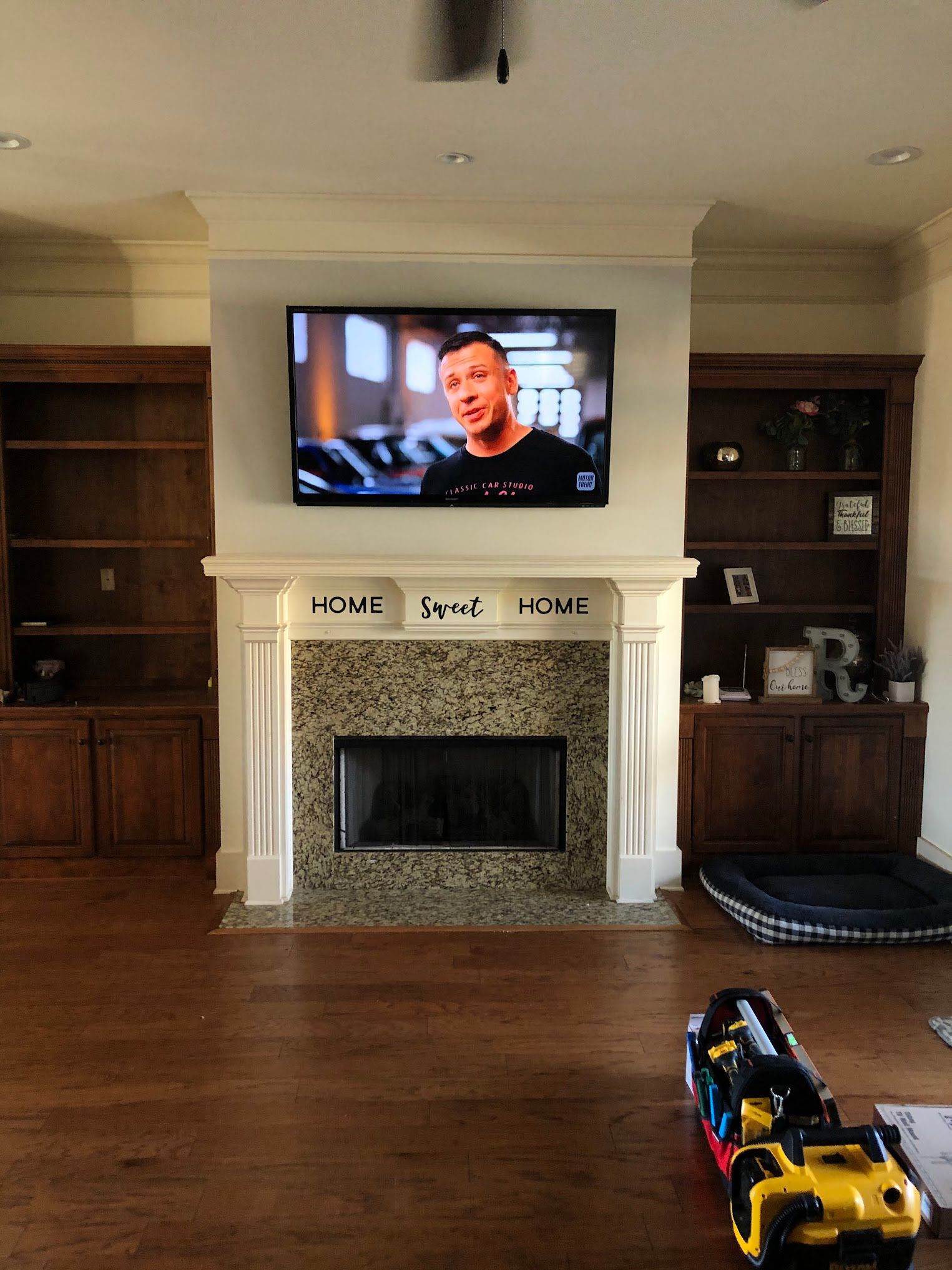 A TV mounted above a fireplace, flanked by bookshelves in a living room, with a toy in the foreground.