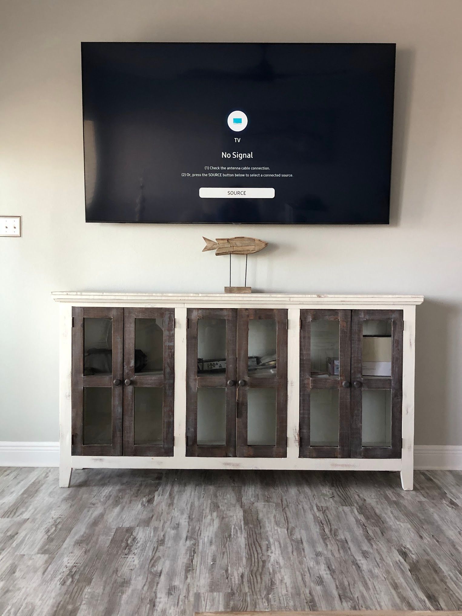 TV mounted above white and brown cabinet, wooden fish decoration.