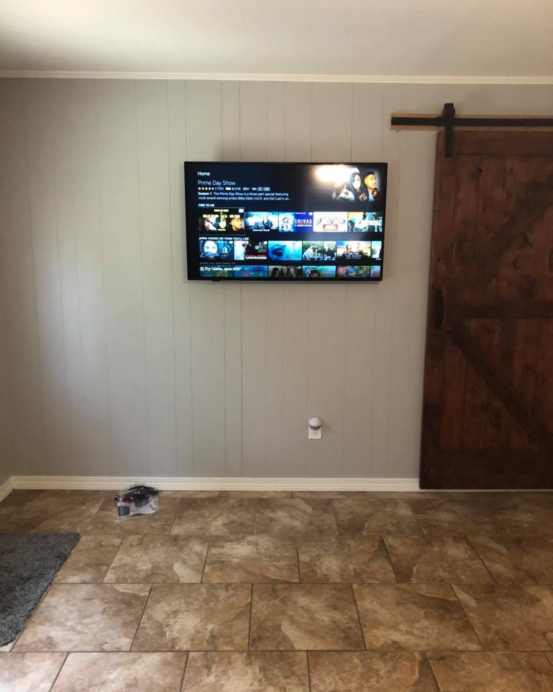 A TV mounted on a gray paneled wall next to a sliding barn door.