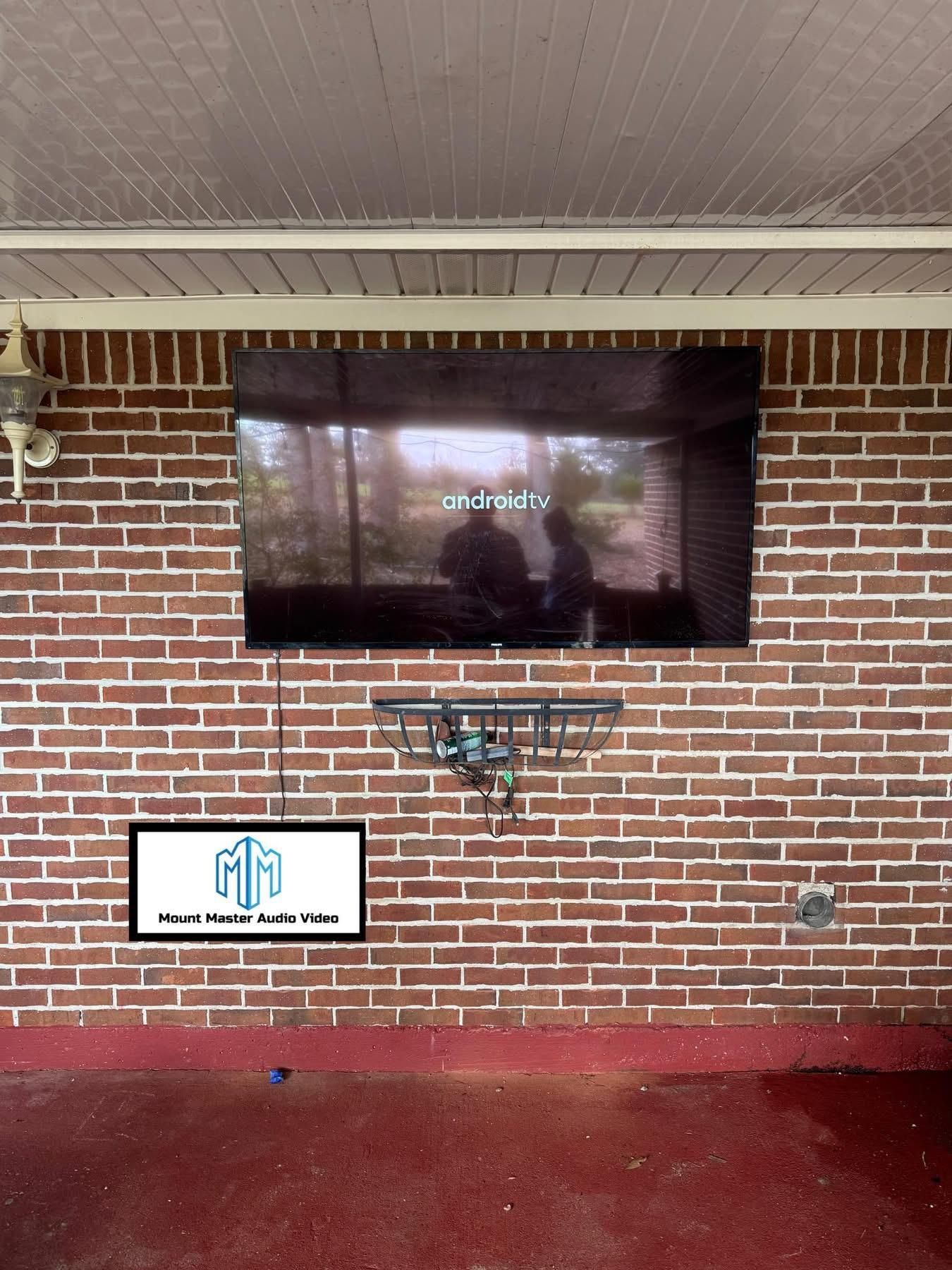 TV mounted on a red brick wall on an outdoor patio, with a lower utility bar.