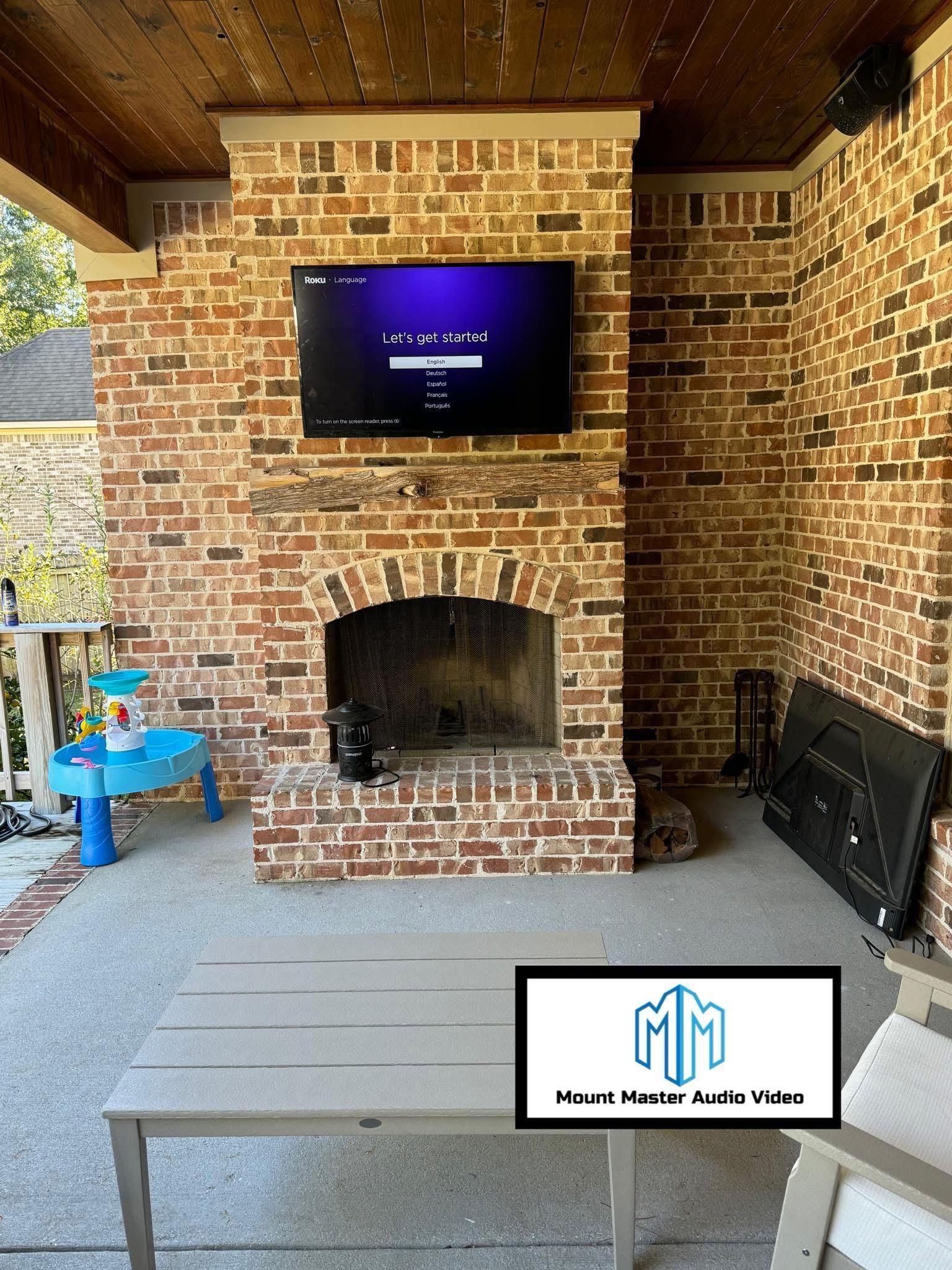 Outdoor brick fireplace with mounted TV; patio furniture and blue table.
