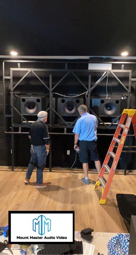 Two men installing a large speaker in a soundproofed room.