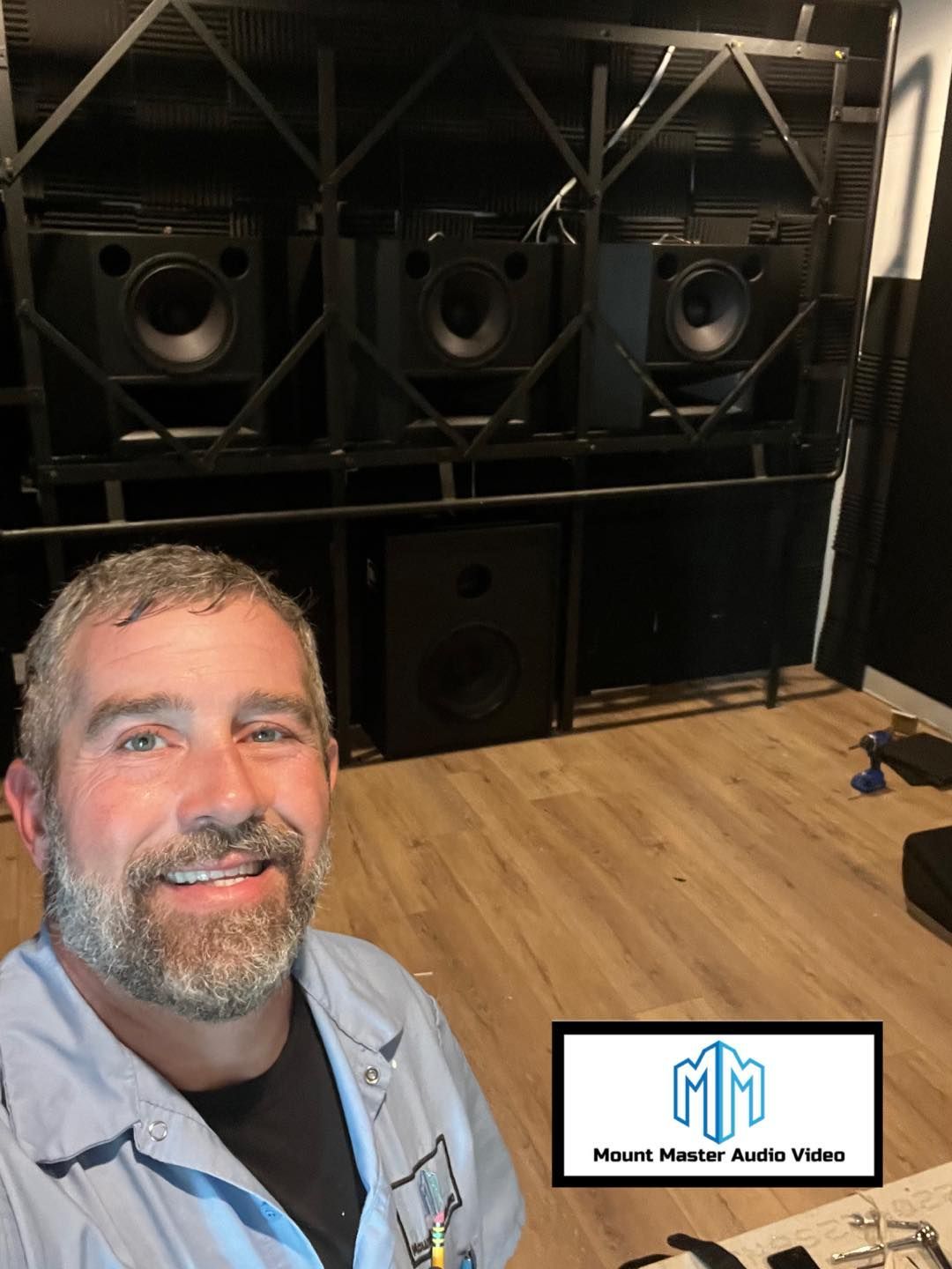 Man smiles at the camera; large speakers in a custom frame sit behind him.