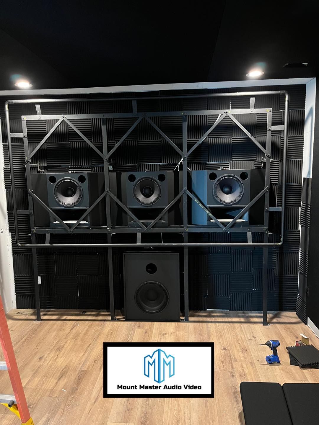 Black speaker setup in room with acoustic foam, metal frame, and logo on floor.
