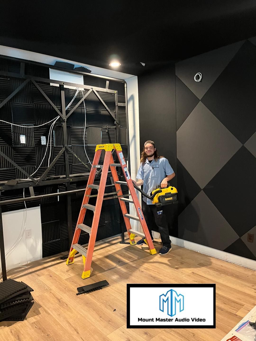 Man with saw stands by ladder, black and gray soundproofing in studio.