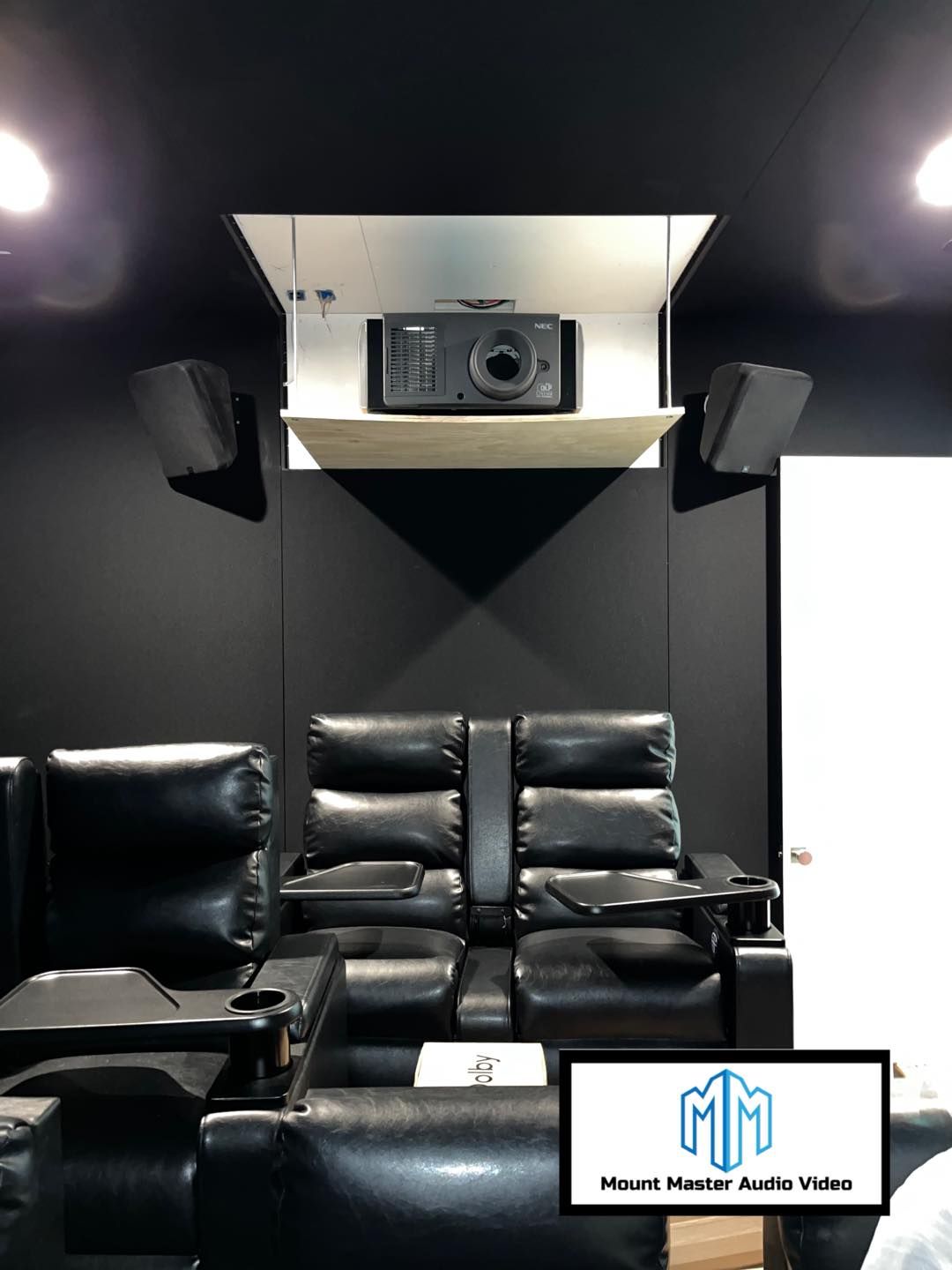 Home theater: black leather recliners, projector in ceiling, speakers, black walls, white door.