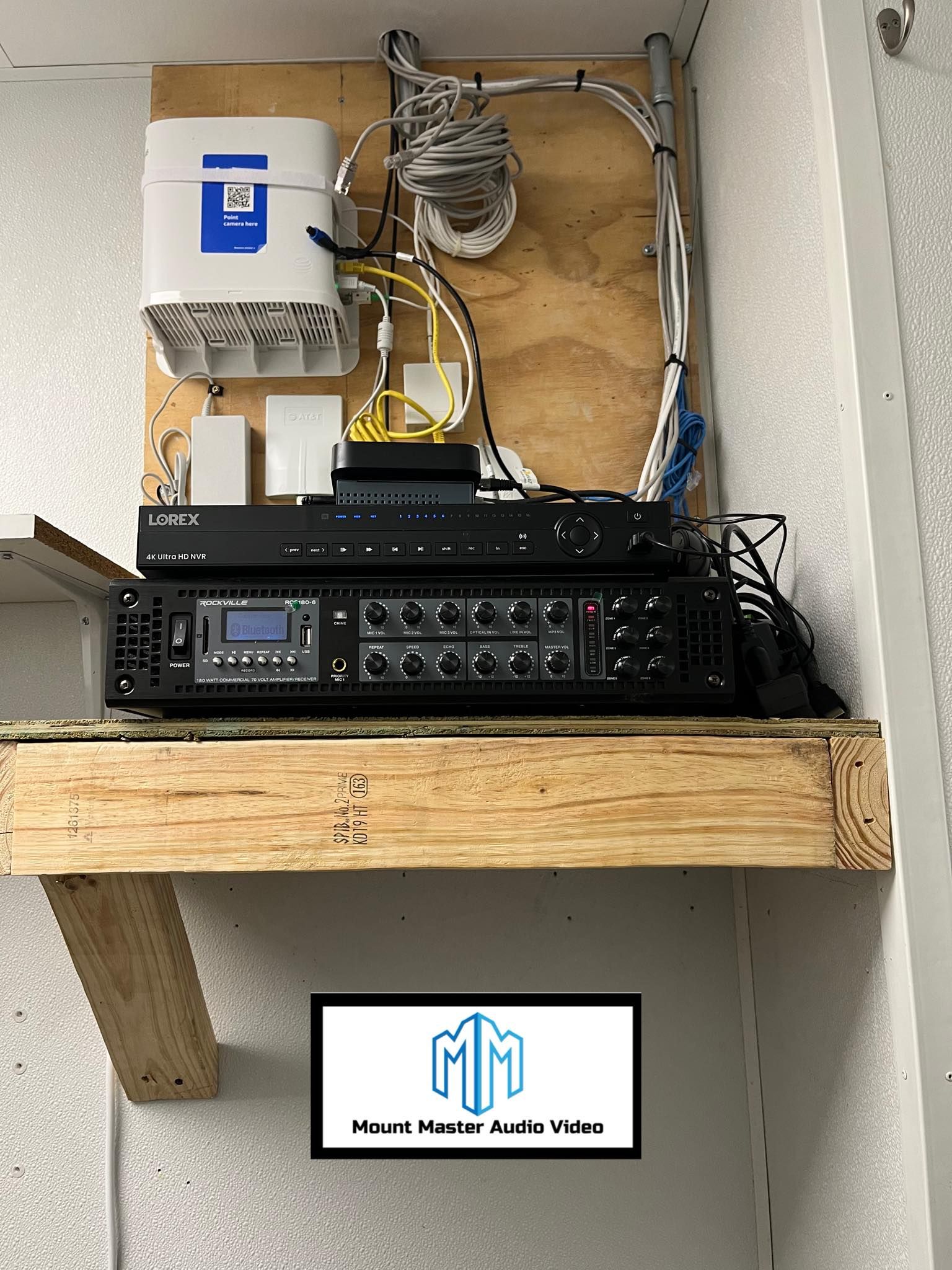 Network equipment and audio system on a wooden shelf, mounted on a white wall.