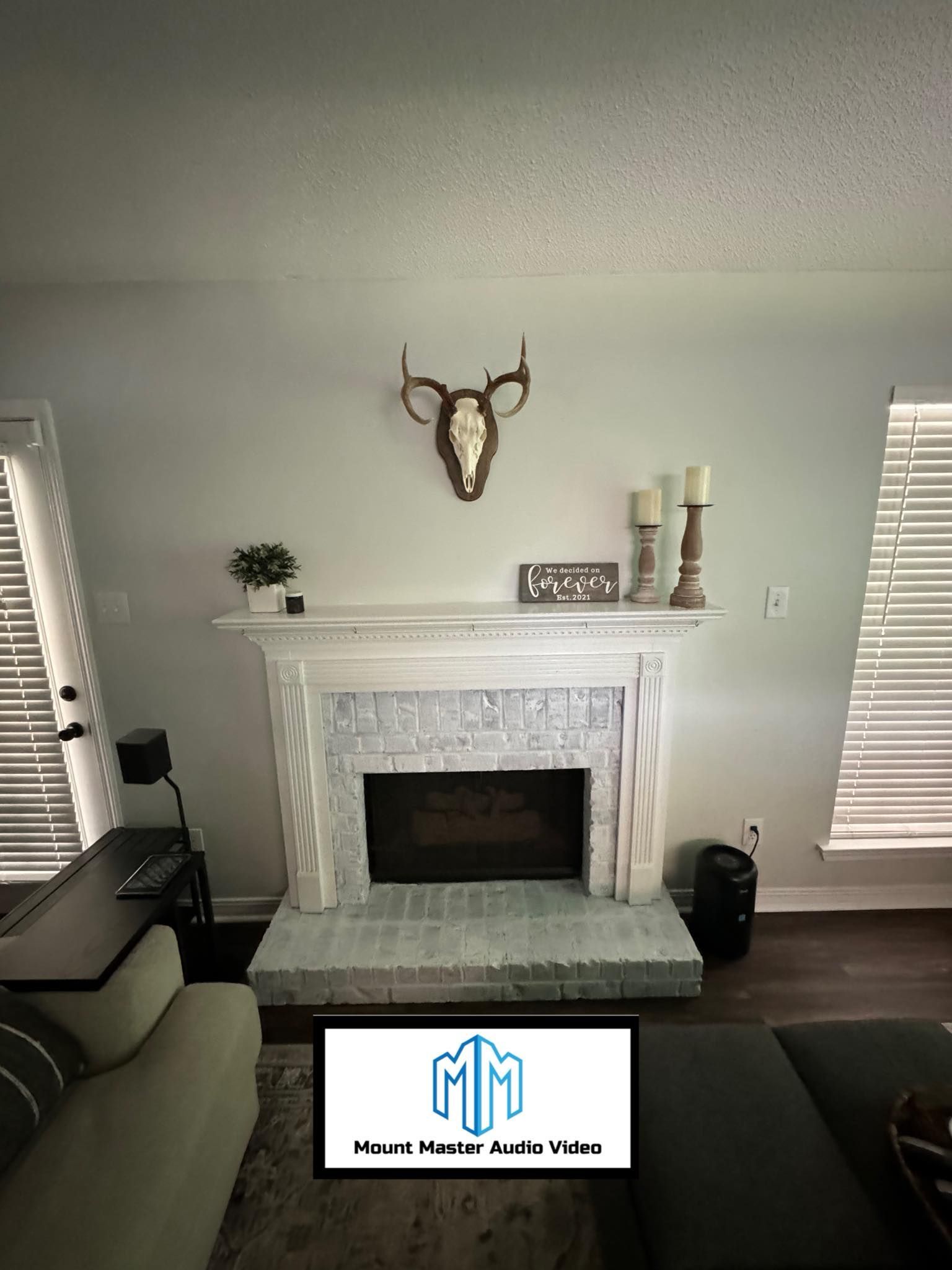 Fireplace with deer skull and candles, desk to the left, and a window.