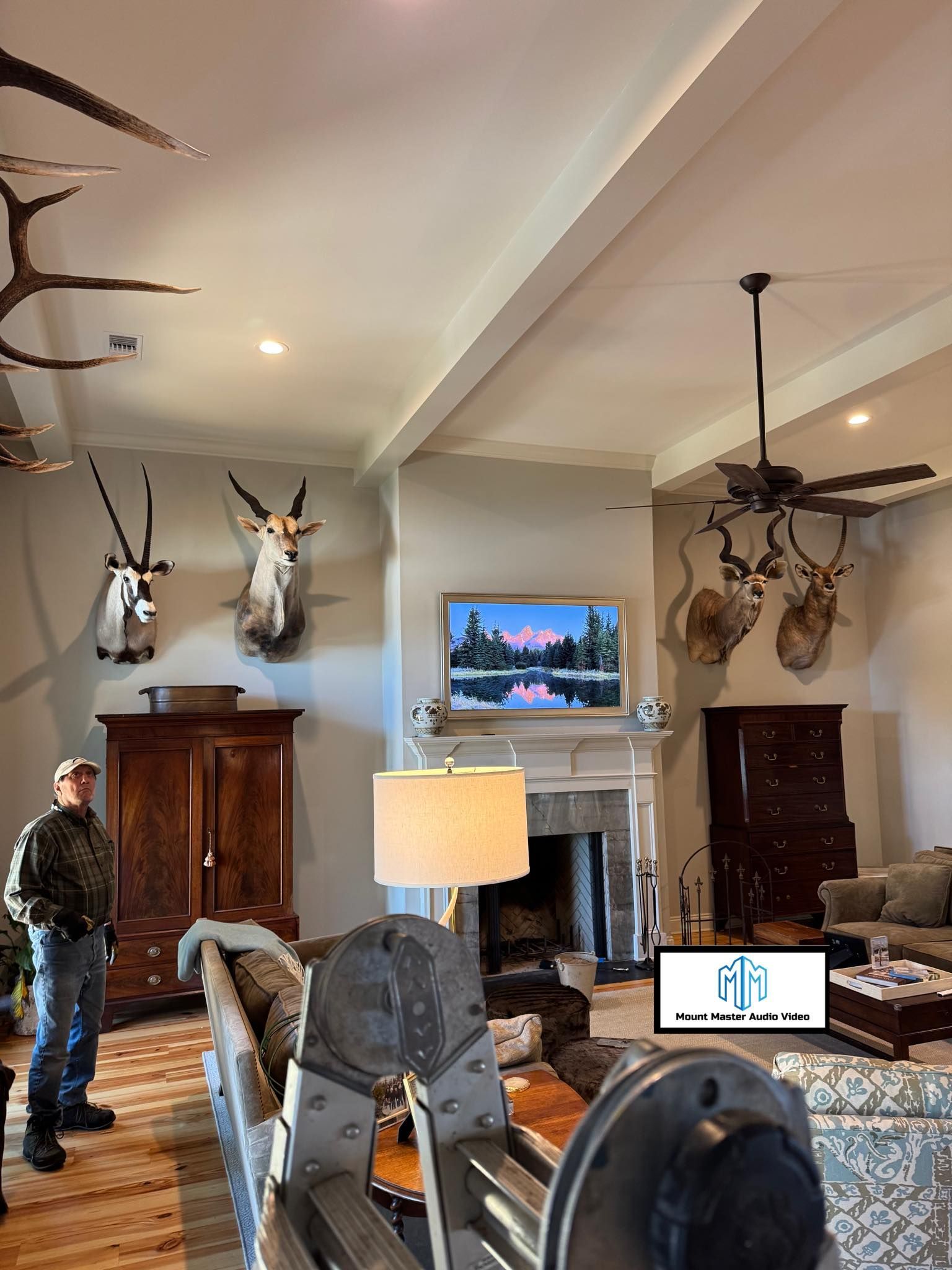 Living room with taxidermied animal heads, fireplace with TV, person standing, and rustic furniture.
