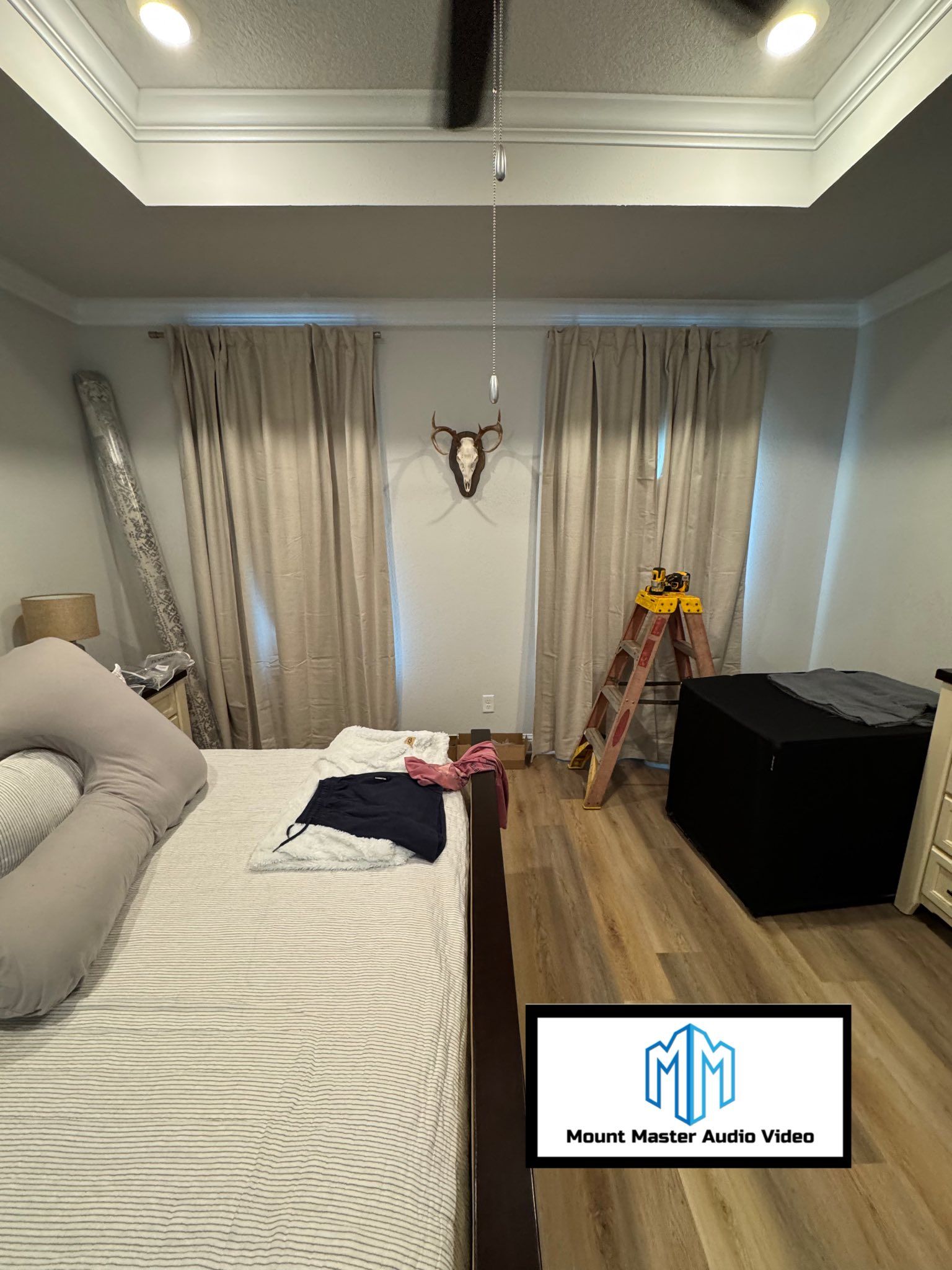 Bedroom with bed, curtains, ladder, and a decorative deer head on the wall.