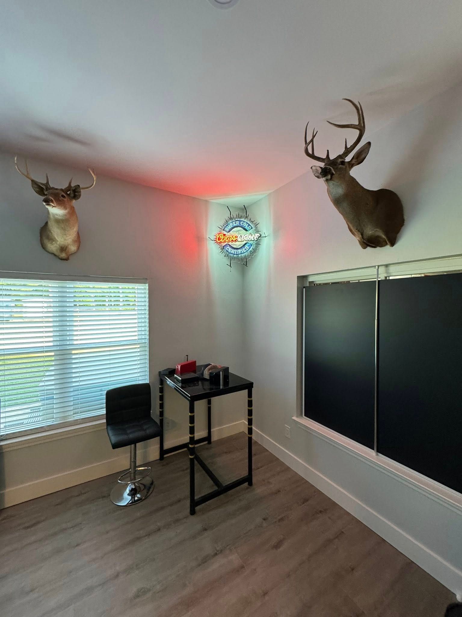 Room with deer heads, window, desk, chair. Red light fixture in the corner.