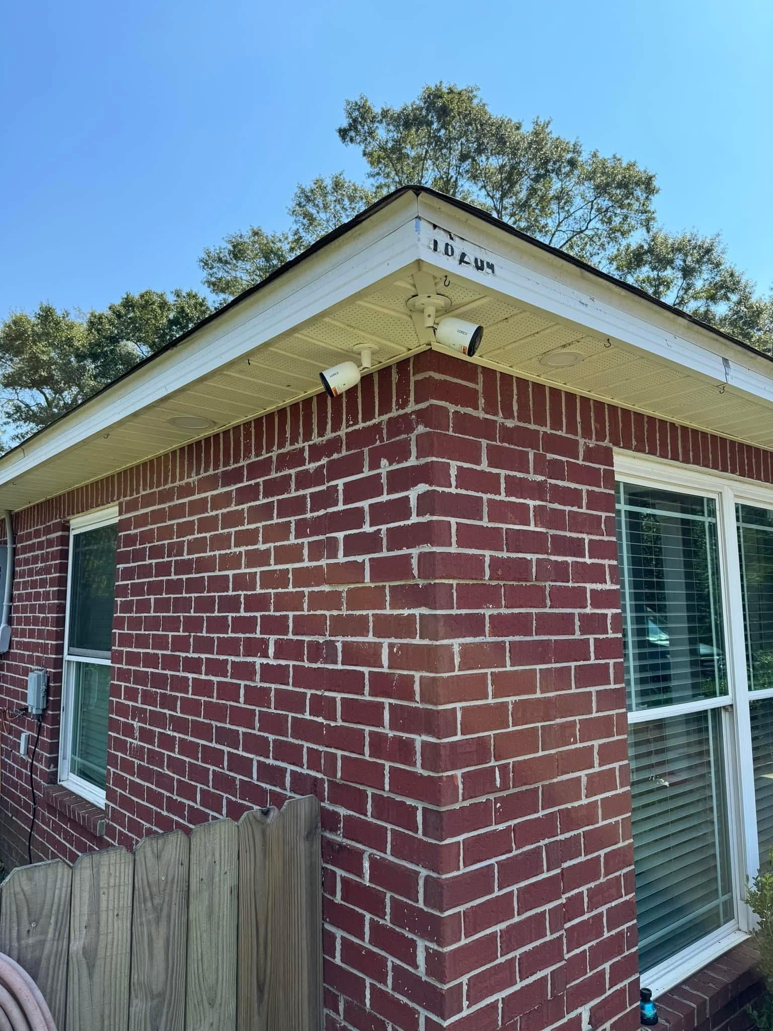 Red brick building corner with two security cameras, a white roof, and windows against a clear blue sky.