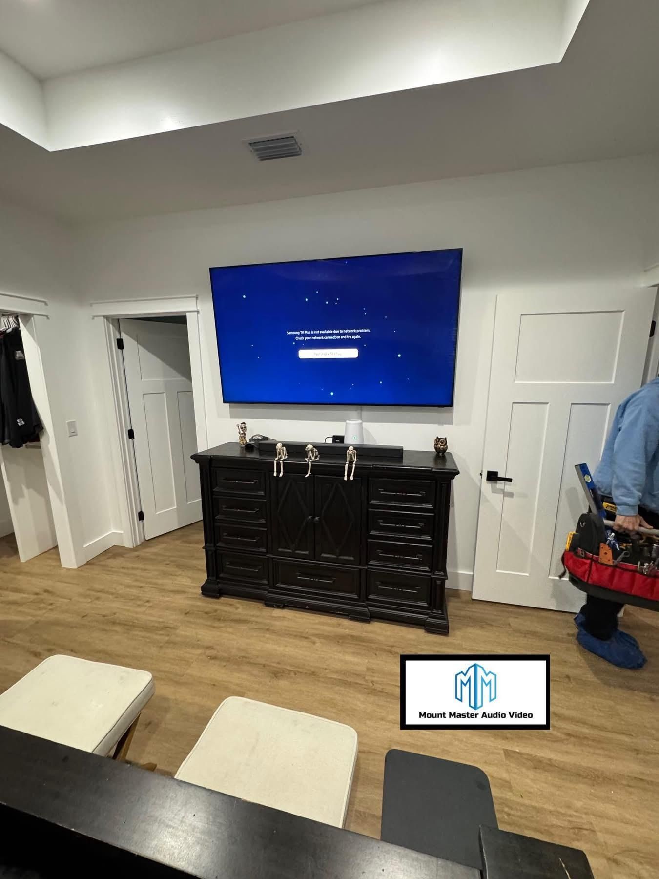 TV mounted above a dark cabinet, two white doors, a light wooden floor, and a person in the right corner.