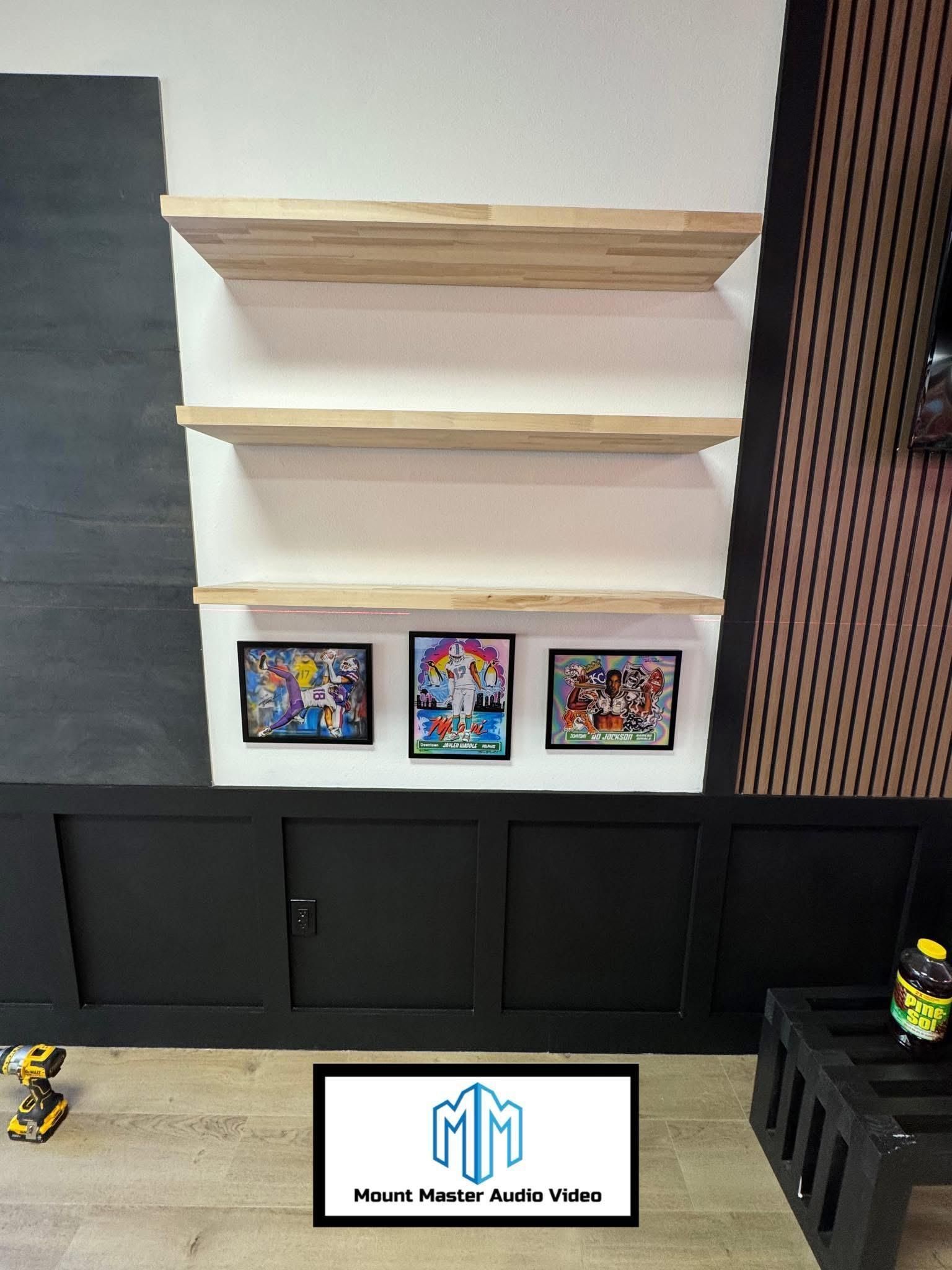 Shelves with framed art above a black cabinet and accent wall.