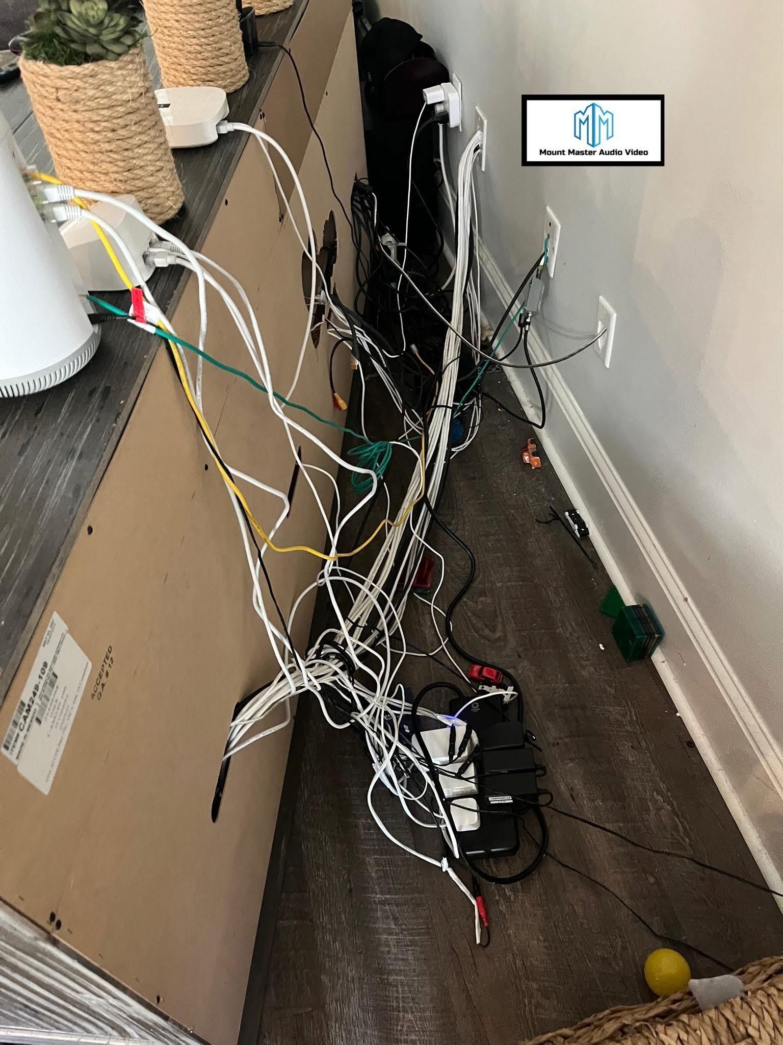 A tangle of white, black, and colored cords behind a cabinet, near a wall and floor.