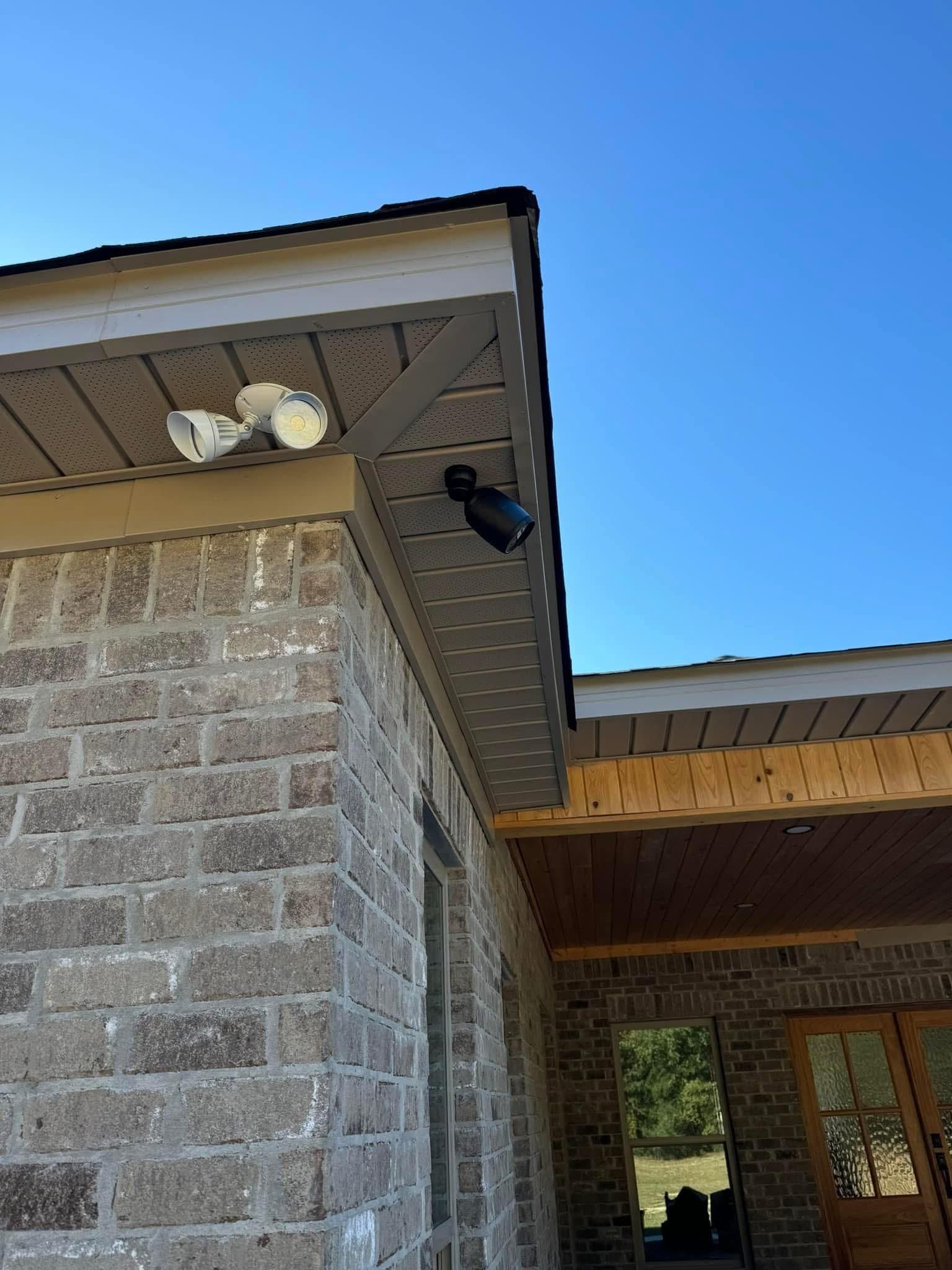 Brick building exterior with security lights under the roof's overhang. Clear blue sky.