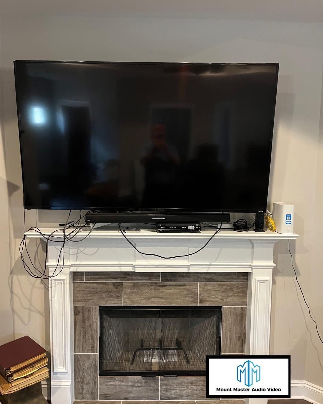 Large TV over fireplace with exposed wires and components on mantel.