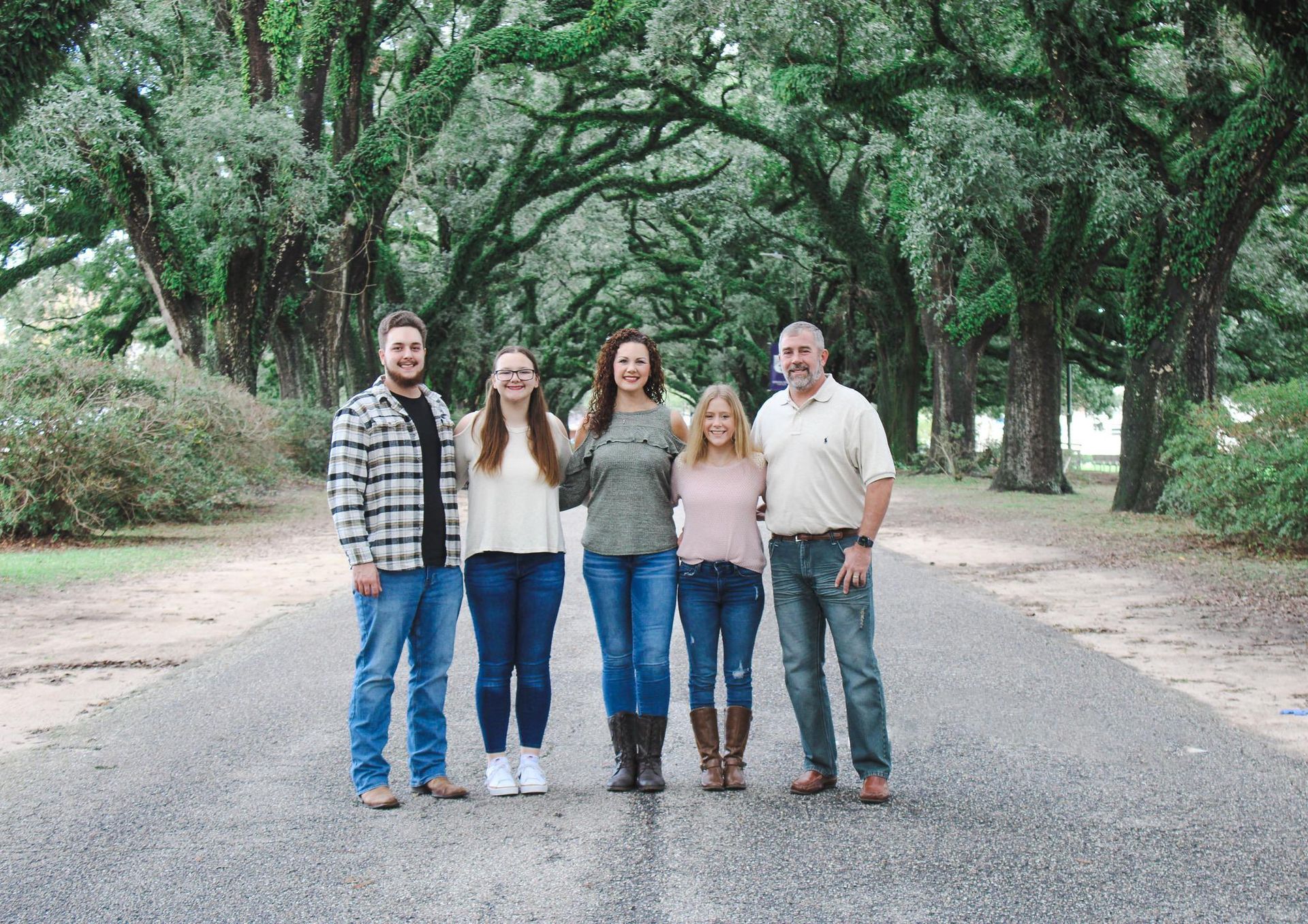 Family of five standing on a tree-lined road; they smile.