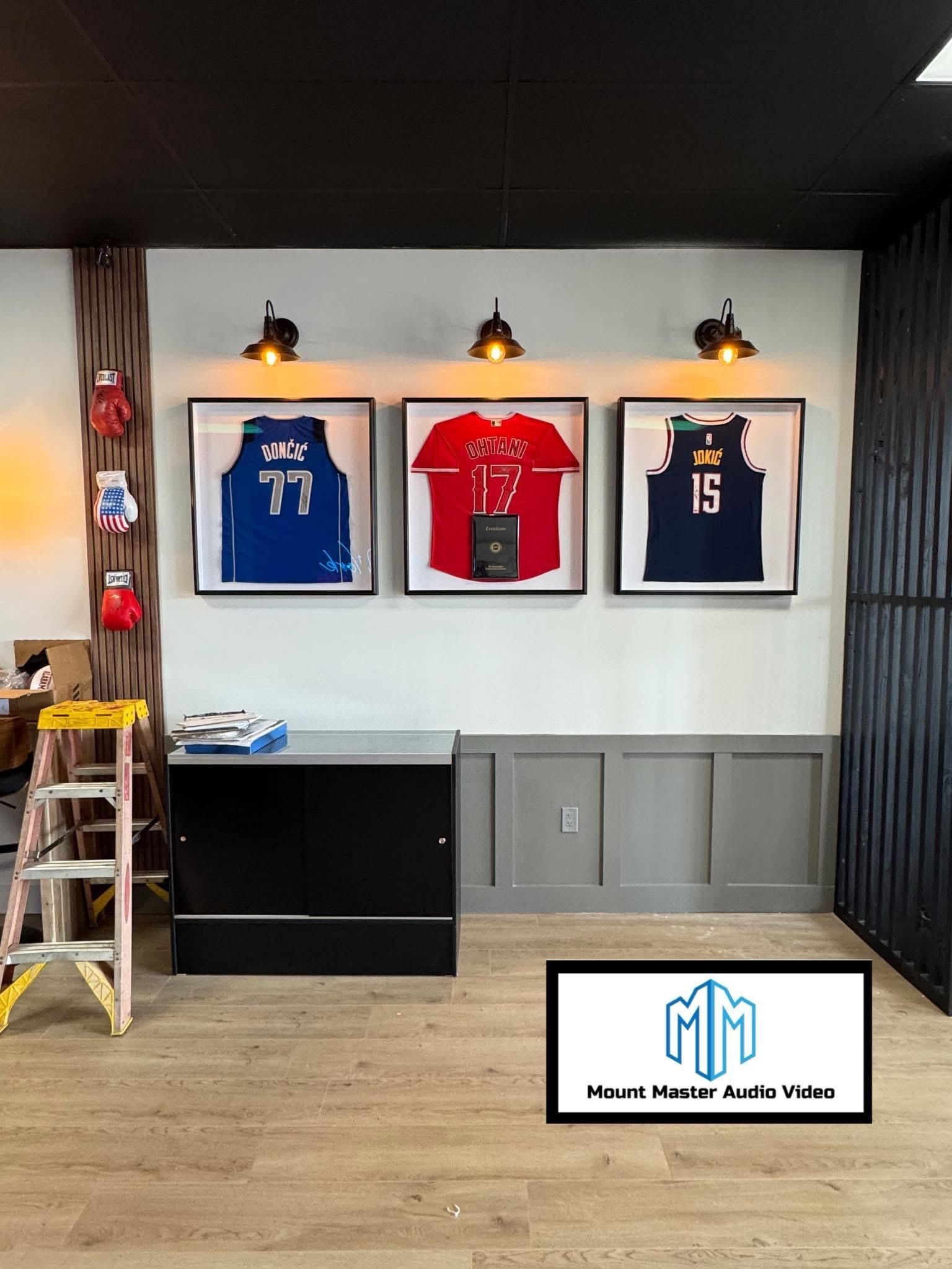 Framed pixelated jerseys on a wall with spotlights; a black cabinet and logo are in the foreground.
