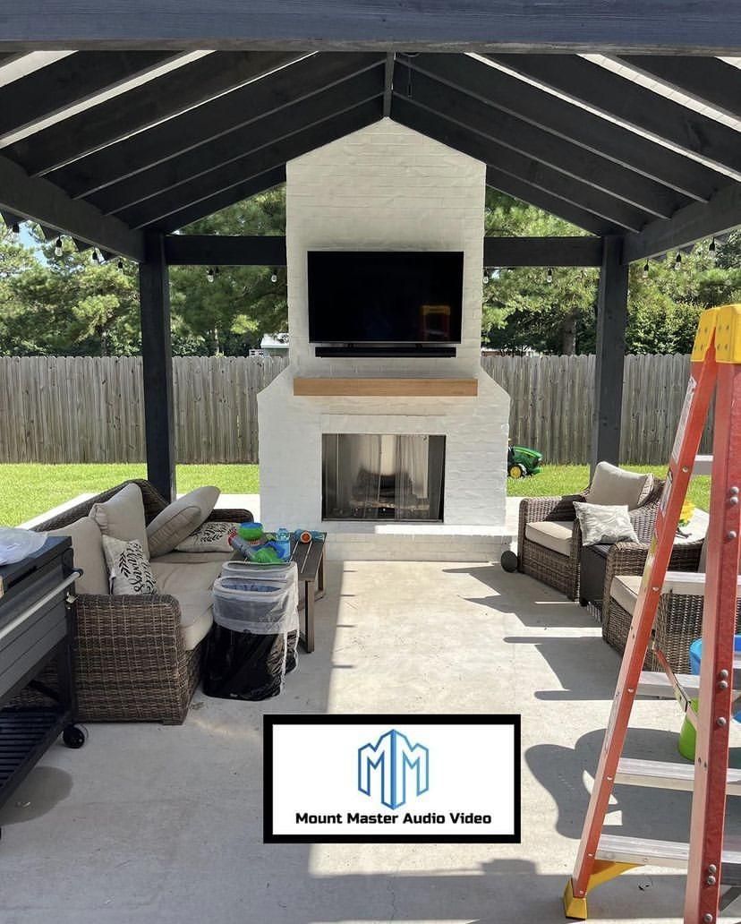 Outdoor living space with a white brick fireplace, TV, and black pergola.