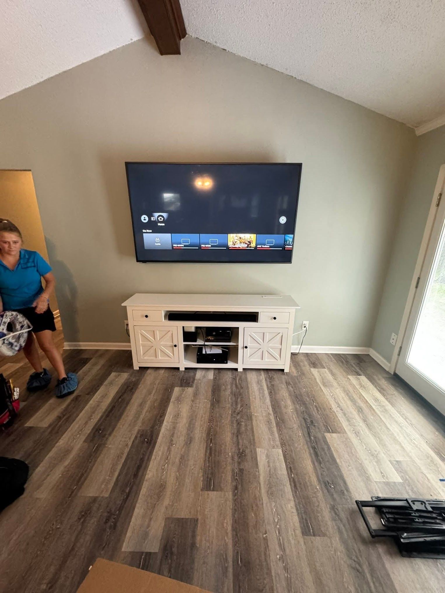 A TV mounted above a white cabinet in a living room; a person stands nearby.