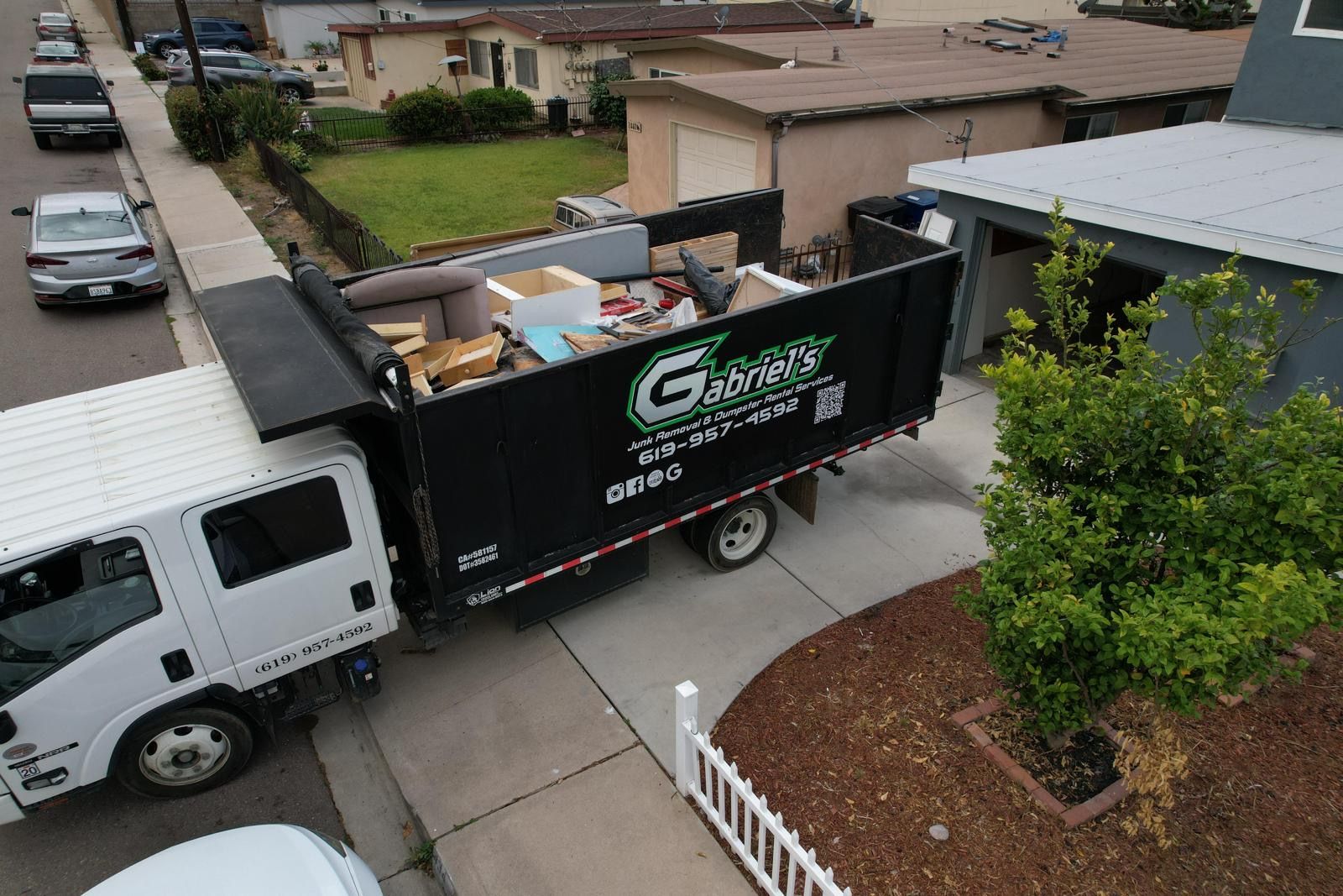 An aerial view of a dumpster truck filled with furniture in a driveway.