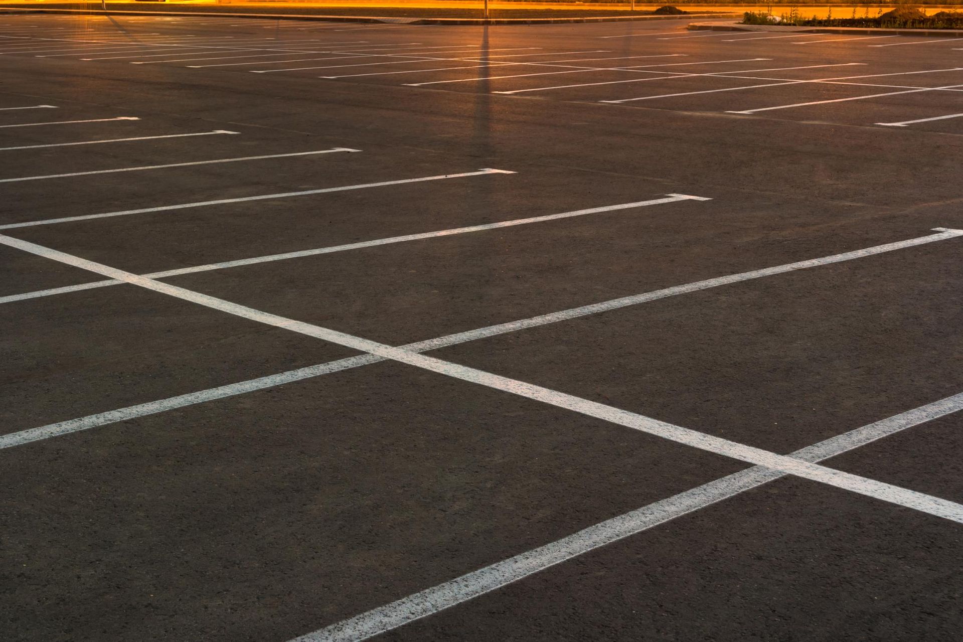 An empty parking lot at sunset, showing rows of white painted lines on asphalt.