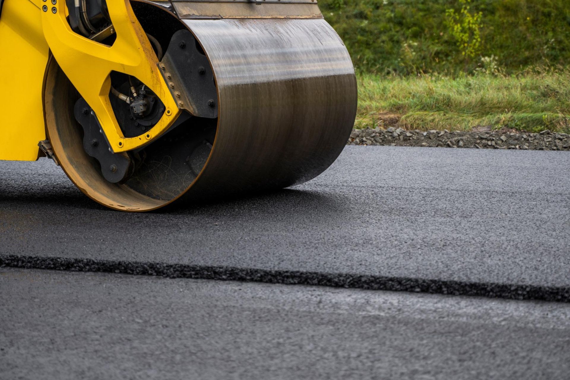 A yellow road roller compacts freshly laid dark asphalt on a construction site.