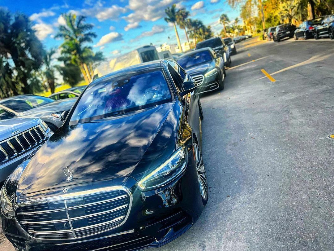 Black Mercedes sedan parked on a street lined with other vehicles, under a sunny sky.