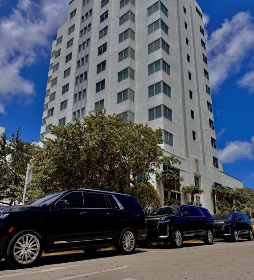 Black SUVs parked in front of a tall white building on a sunny day.