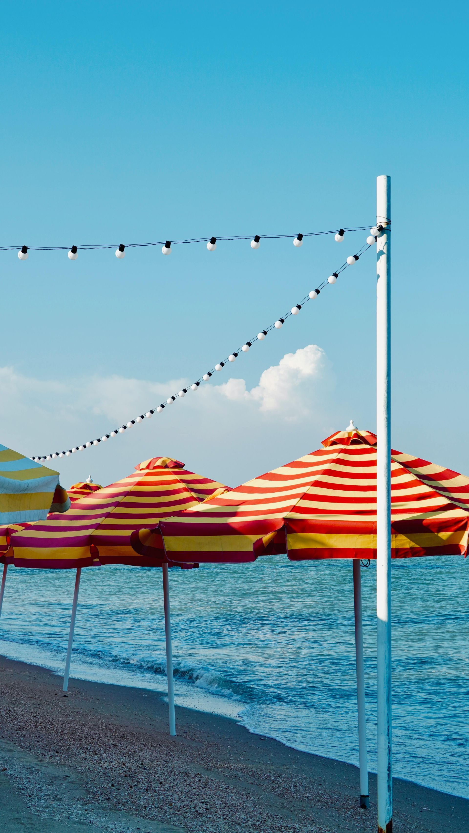 Beach umbrellas with red and yellow stripes on a pebbled beach, ocean in the background, blue sky.