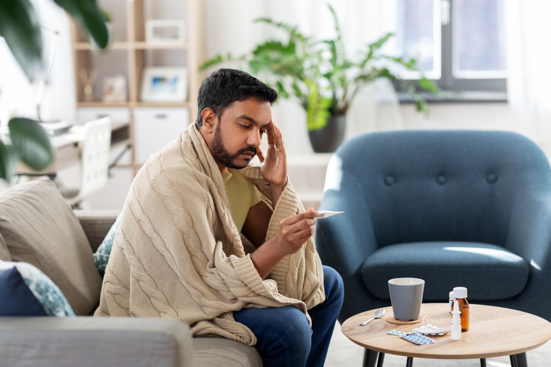 A man is sitting on a couch with a thermometer in his hand.