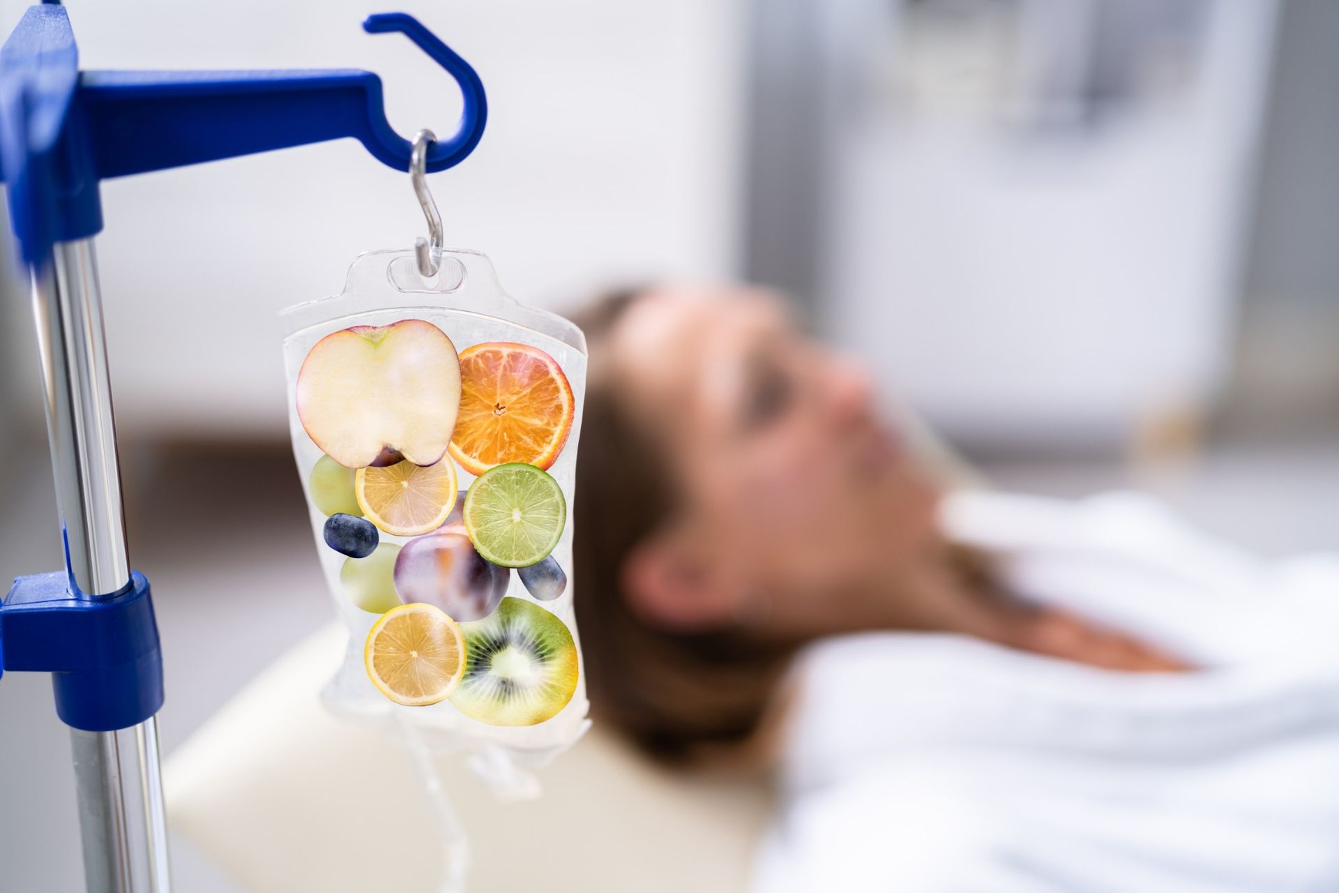 A woman is laying in a hospital bed with an IV bag of fruit hanging from a pole