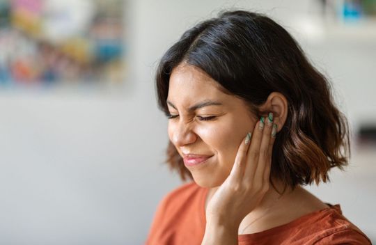 A woman is holding her ear because she has a toothache.