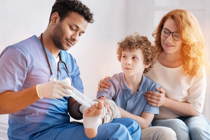 A doctor is bandaging a child 's foot while a woman looks on.