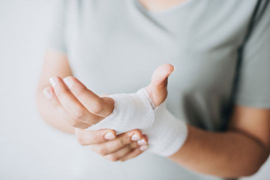 A woman is holding her wrist with a bandage on it