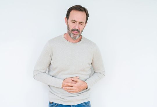 A man with a beard is holding his stomach in pain.