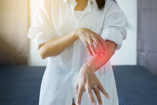 A woman is scratching her elbow with a red spot on it.