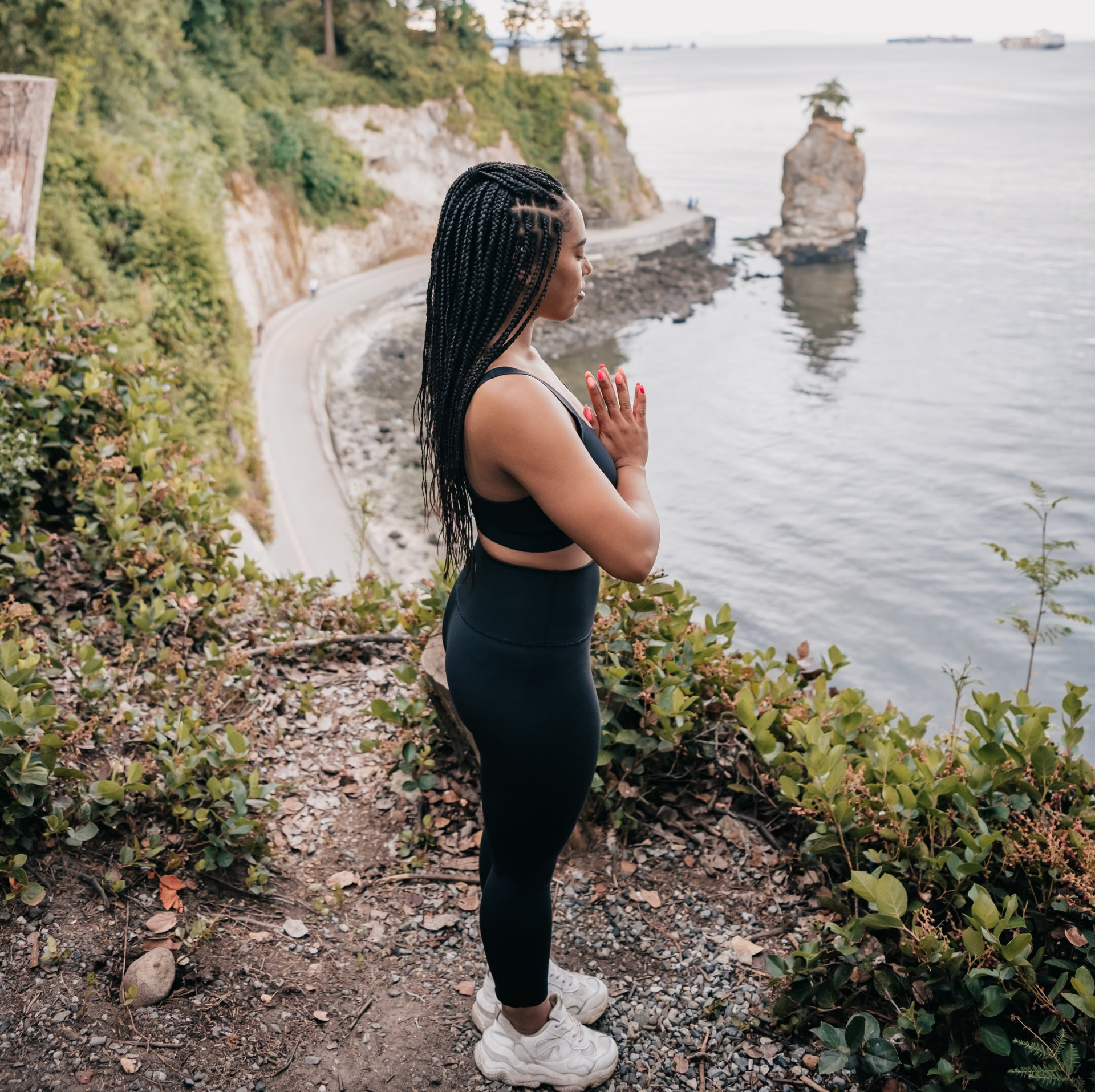 A woman is standing on a cliff overlooking a body of water.