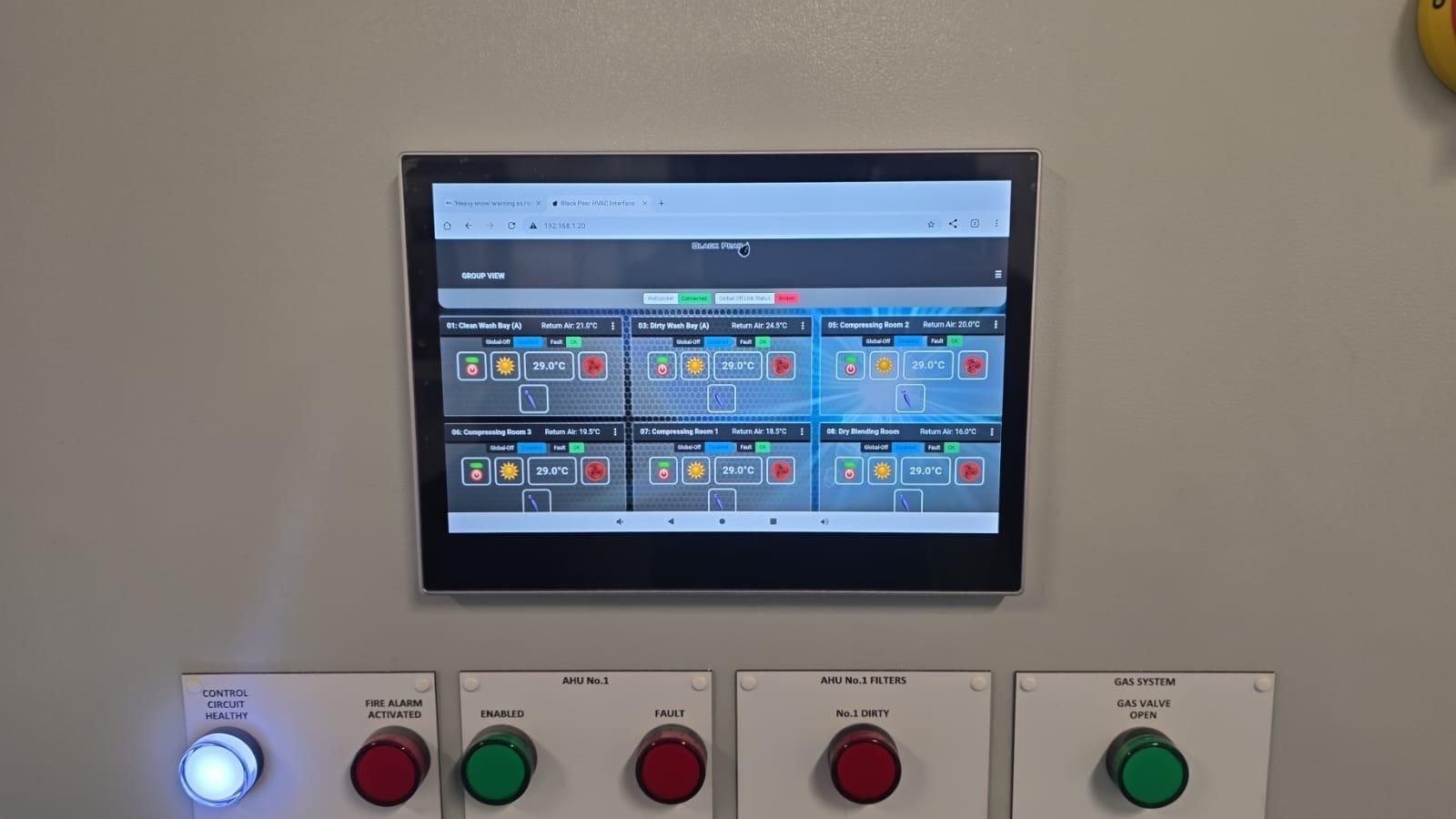 Wall-mounted control panel with a small monitor and illuminated red and green buttons beneath it.