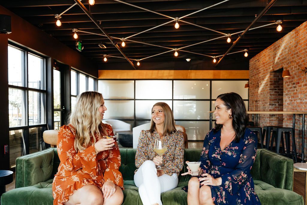 Three Women Sitting & Holding Cocktails in Six-Mile Ordinary, a Spirits Bar in Columbia, MO. 
