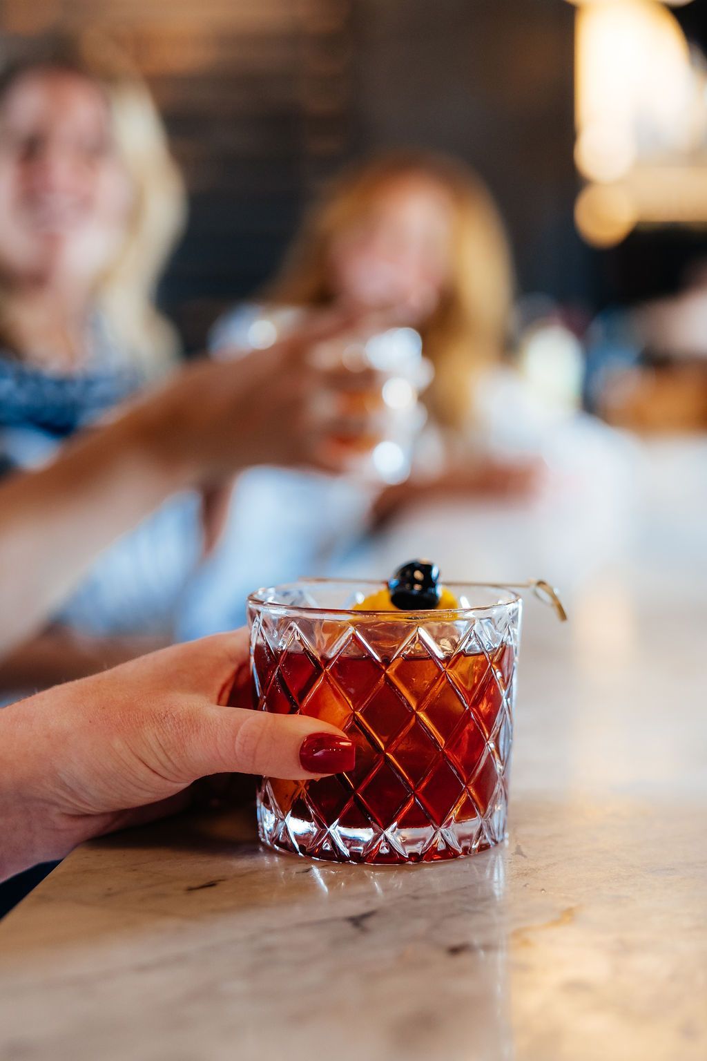 Closeup of Six-Mile Ordinary Cocktail With People Sipping Their Drinks in the Background. 